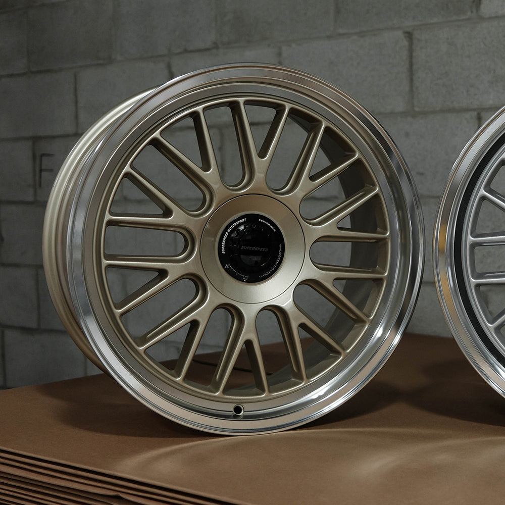 Close-up of a metallic alloy wheel on a textured surface with a gray brick wall background.